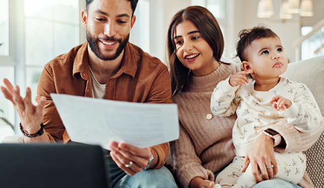 A couple and a baby sit on a couch looking at a document