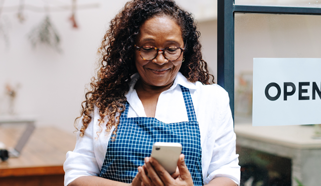 A woman wearing an apron looks at her phone outside a shop