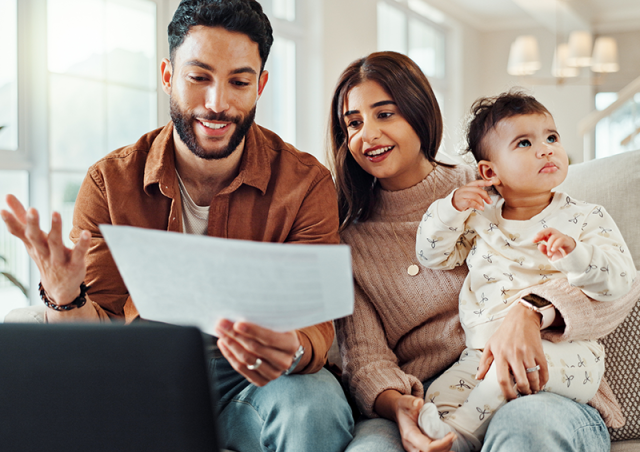 A couple and a baby sit on a couch looking at a document