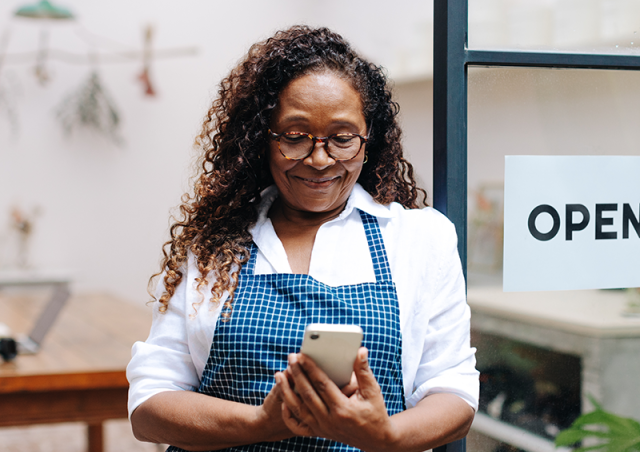 A woman wearing an apron looks at her phone outside a shop